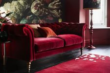 a moody and refined living room with a bold floral mural, a deep red sofa, a floral rug, floral lamps and burgundy walls