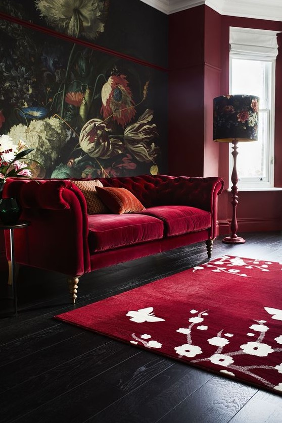 a moody and refined living room with a bold floral mural, a deep red sofa, a floral rug, floral lamps and burgundy walls