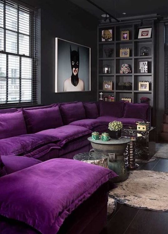 a moody contemporary living room done in black and graphite grey, a built-in shelf for displaying, a purple sectional and a statement artwork