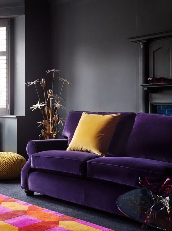 a moody living room in dark greys spruced up with a deep purple sofa, yellow pillows and a colorful geometric rug