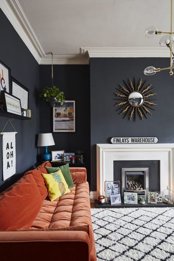 a moody living room with a faux fireplace, artworks, prints and candles, a rust-colored sofa and a pretty gallery wall