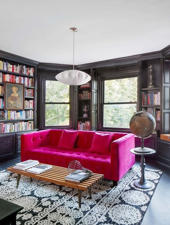a moody room with a bay window, built-in bookshelves, a hot pink tufted sofa for a color accent in the space