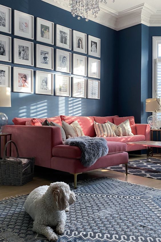 a navy living room with a pink sofa, some side tables, a grid gallery wall, printed rugs and a crystal chandelier and a cool lamp