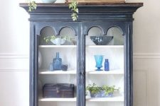 a navy shabby chic cabinet with glass doors and beautiful accessories on display, with pillows on top and greenery in a vase is amazing
