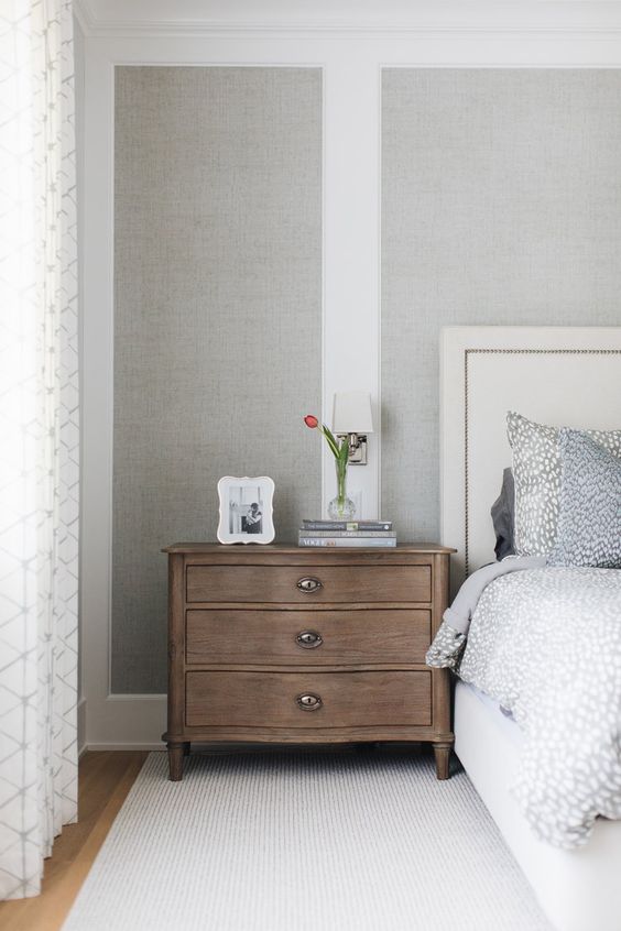 a neutral bedroom with grey grasscloth wallpaper, a stained nightstand, a white bed with grey bedding is soothing and cool