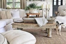a neutral rustic living room with rough wooden tables, a stool, some whitewashed candleholders and a jute rug