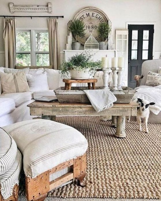 a neutral rustic living room with rough wooden tables, a stool, some whitewashed candleholders and a jute rug