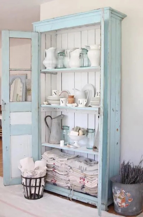 a pastel blue cupboard with white boards inside is used for storing dinnerware, pitchers and kitchen towels