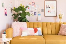 a pastel living room with a yellow sofa, blush walls, a colorful and fun gallery wall and a potted plant