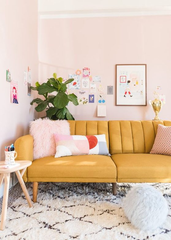 a pastel living room with a yellow sofa, blush walls, a colorful and fun gallery wall and a potted plant