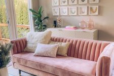 a pretty feminine living room wih taupe walls, a pink sofa, a white and gold dresser, a gallery wall of necklaces, greenery and books