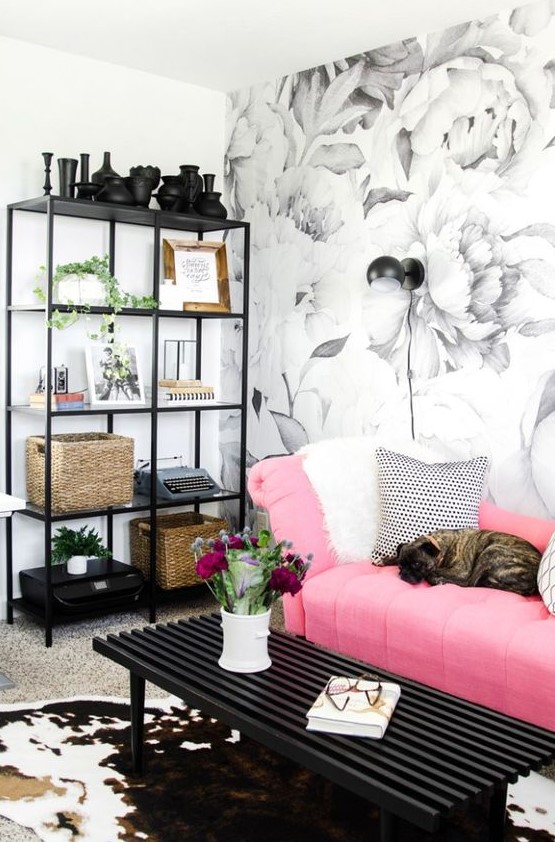 a pretty monochromatic living room with a floral wall, a storage unit, a black table and a bright pink sofa with printed pillows