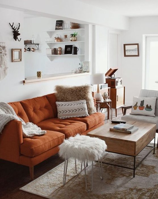 a pretty neutral living room in boho style, with a rust colored sofa, a low table and a fur stool, printed textiles is very welcoming