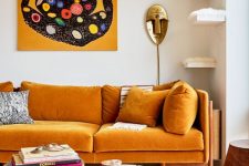 a refined and chic living room with a mellow yellow sofa with pillows, a duo of round coffee tables, a bold artwork and a gold mask lamp