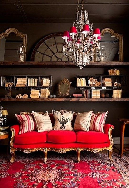 a refined eclectic living room with dark walls, dark stained shelves, a refined gold and red sofa and a catchy chandelier