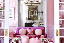 a refined feminine living room with pink walls, a pink loveseat, floral chairs, blush coffee tables and pillows and a chic chandelier