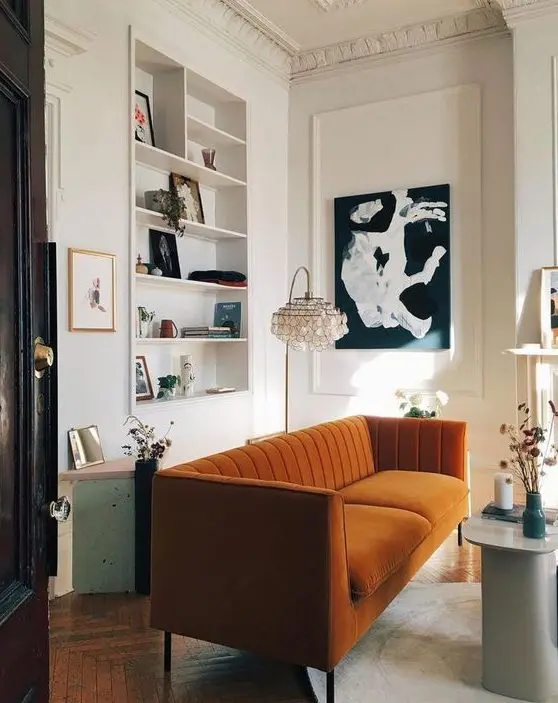 a refined living room with a niche with built in shelves, a rust colored sofa, a black and white artwork and dried blooms