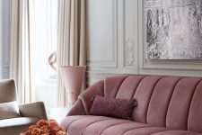 a refined living room with molding, a dusty pink sofa, a duo of black coffee tables, a creamy chair, some blooms and some books