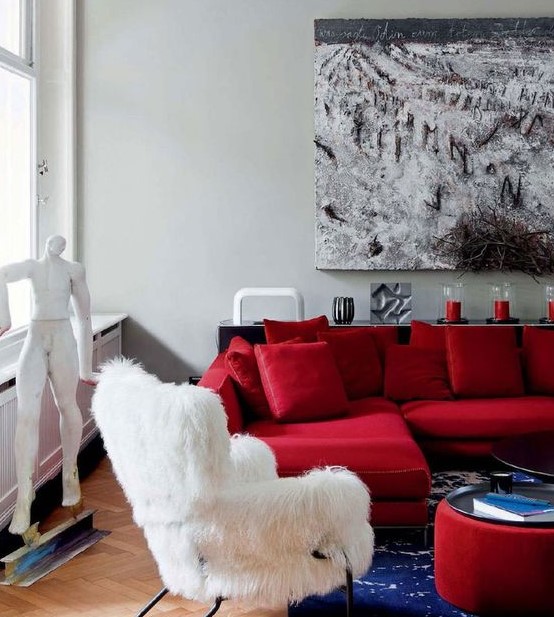 a refined modern living room with a hot red sectional, a white faux fur chair, a bold red ottoman and a creative artwork