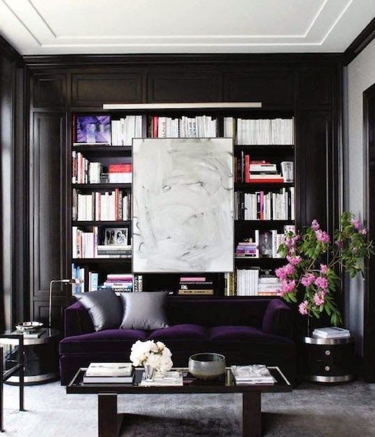 a refined modern monochromatic living room with built in bookshelves, a deep purple velvet sofa for a color statement and a chic table