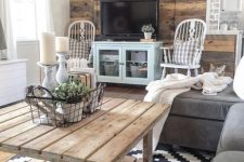 a rustic living room with a reclaimed wood wall, a wooden table, grey and blue furniture and refined vintage chairs