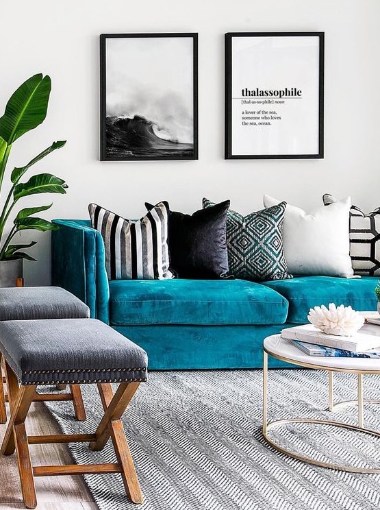 a seaside living room with a turquoise sofa, printed pillows, a black and white gallery wall, grey stools and a round table