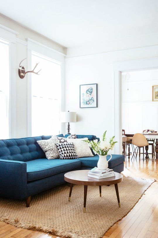 a simple and lovely living room with a blue sofa, a jute rug, a round table and printed pillows is a welcoming space
