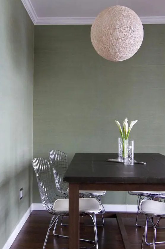a simple dining space with green grasscloth wallpaper, a dark-stained table, wire chairs and a yarn ball lamp