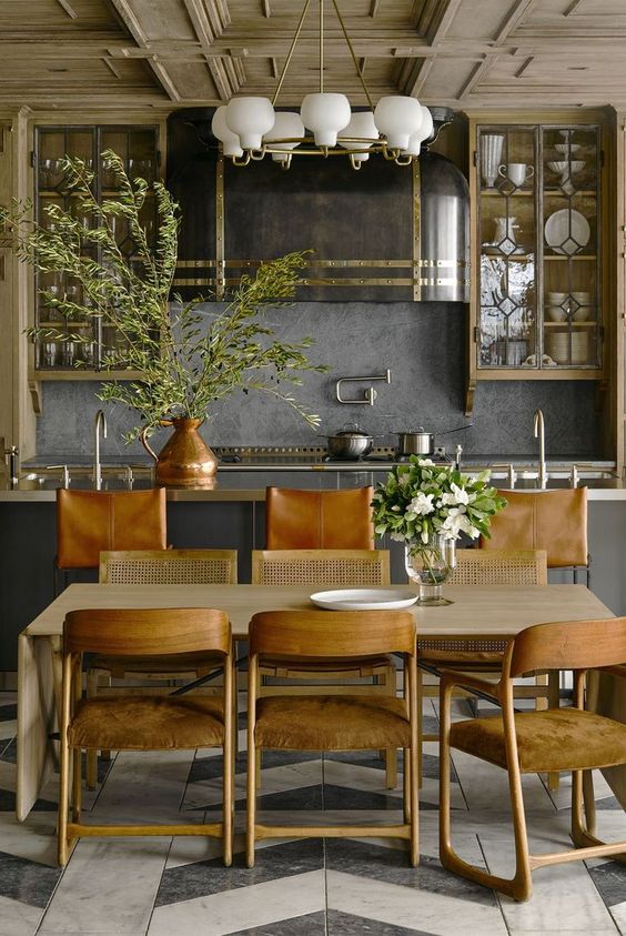 a slate grey kitchen with a stone backsplash, a light-stained cabinet, a kitchen island, a chandelier and amber chairs