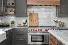 a slate grey kitchen with shaker cabinets, white skinny tiles, a wooden kitchen island and a wooden hood plus a bold rug