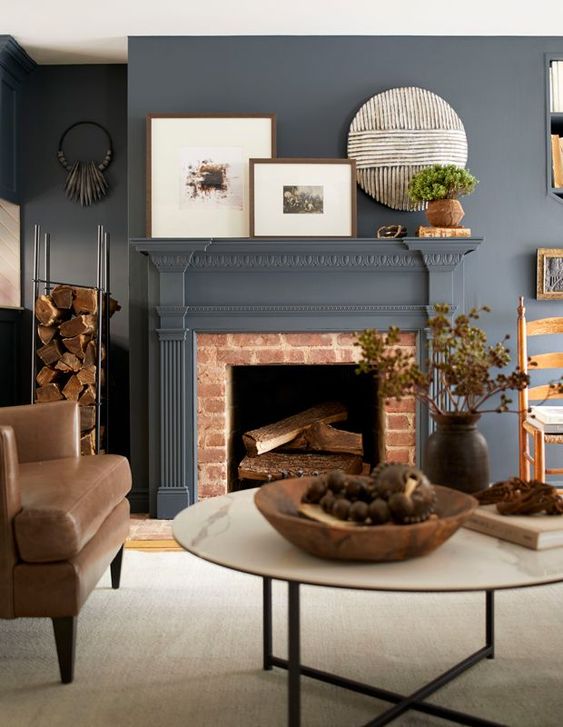 a slate grey living room and a non-working fireplace, leather chairs, a round coffee table and artworks