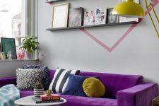 a small and cool living room with grey walls, ledges with a gallery wall, a bold purple sectional sofa, a duo of coffee tables and a striped rug