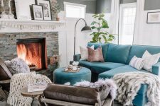 a small living room with grey walls, a fireplace clad with faux stone, a turquoise sofa with a pouf, leather chairs and blankets