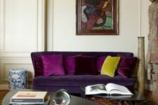 a sophisticated living room with a deep purple sofa, black coffee tables, wicker chairs, bold textiles and an artwork