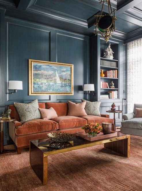 a sophisticated living room with navy walls, a rust colored velvet sofa, a low polished table, built in shelves