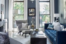 a sophisticated modern living room with grey walls, a navy sofa, a coffee table, a creamy chair with a footrest and a chic chandelier