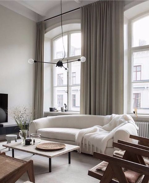 a stylish Scandinavian living room with a modern chandelier, a creamy curved sofa, cane chairs, wooden tables and grey curtains