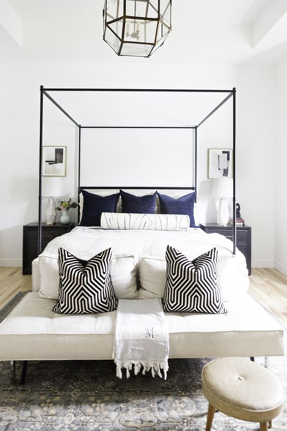 a stylish bedroom with a black frame bed, a large upholstered bench at the foot, a stool and a super cool faceted pendant lamp
