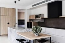 a stylish contemporary kitchen with white lower cabinets, open storage shelves, a black hood, black countertops, light stained wood and a stone kitchen island