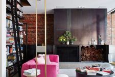 a stylish contemporary living room with a metal fireplace and firewood storage, a hot pink sofa, a neutral one, a large bookcase and gold touches