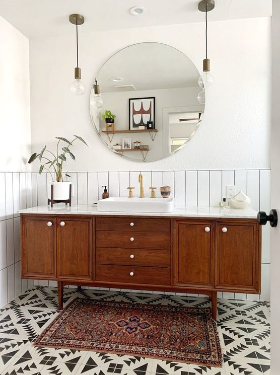 a stylish mid-century modern bathroom with whiet skinny tiles, geo tiles on the floor, a boho rug, a wooden vanity and pendant lamps