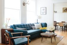 a stylish mid-century modern living room with a blue sectional, a blue chair, a round coffee table, a jute rug and a wooden side table