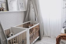 a stylish neutral nursery with white cribs, a rug, grey canopies, a ledge with artworks and lovely textiles