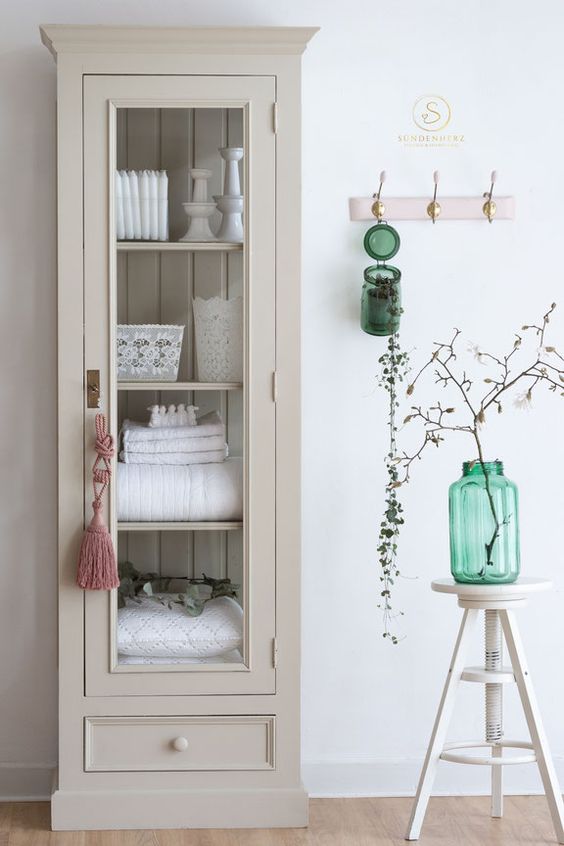 a stylish tan vintage cabinet with a drawer and glass sides and doors to store pillows, towels and other stuff is ideal for a farmhouse space