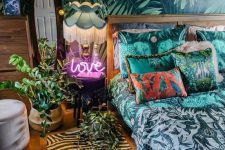 a tropical maximalist bedroom with an accent wall, a gilded bed, a mirror and a neon light plus string lights and bold printed textiles here and there