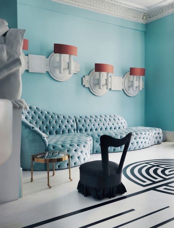 a unique living room with light blue walls and a matching curved sofa, a glass table, a black chair and cool coral and white sconces