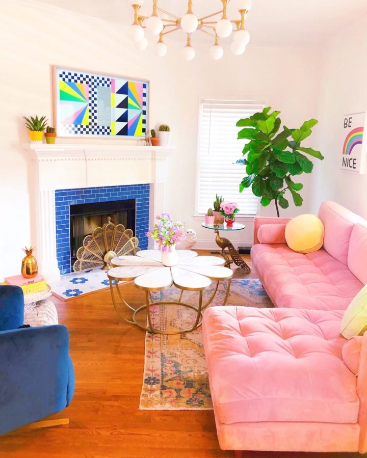a vibrant living room with a fireplace clad with blue tiles, a pink sectional, a blue chair, a glass and a brass coffee table and a bold artwork