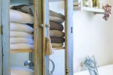 a vintage blue and cream cupboard with chicken wire for storing bathroom towels and other stuff
