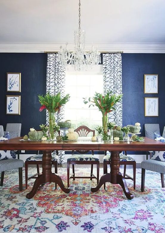 a vintage dining room with navy grasscloth wallpaper, a dark-stained dining table, striped chairs, a crystal chandelier and greenery