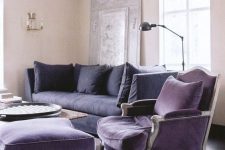 a vintage-inspired living room with tan walls, a deep purple sofa, a purple vintage chair and a footrest, a coffee table and a black floor lamp